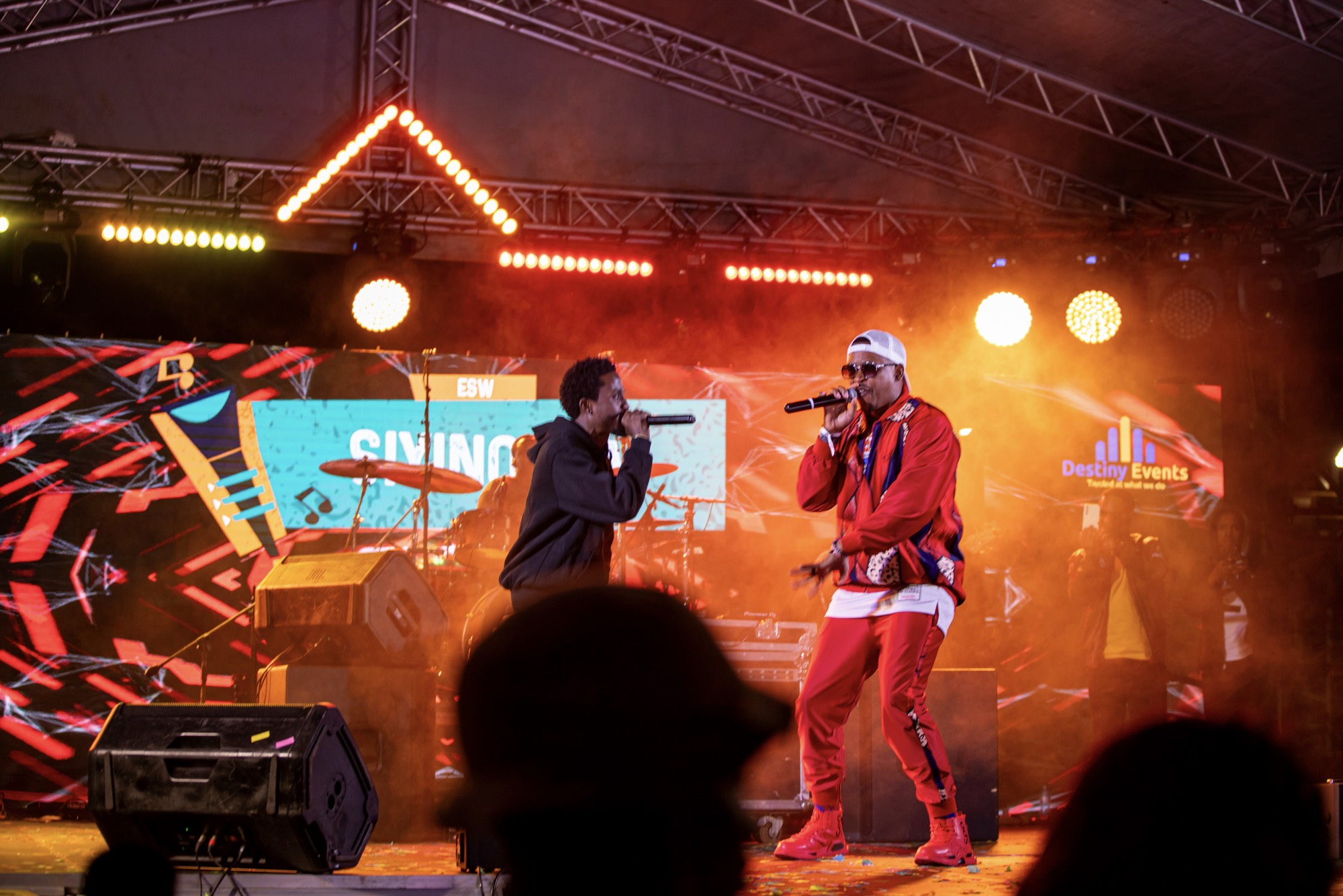 Back of a man at a concert. Hes wearing a beanie hat and a baggy denim jacket with studs. Photo with a purple hue